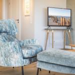 Ein Sessel mit blauem Muster und ein Hocker stehen vor einem Fernseher.