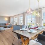Esszimmer mit Holztisch und Sitzgelegenheiten. Wohnbereich mit Sofa und Fenstern.