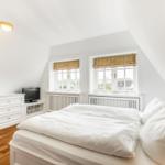 Schlafzimmer mit Doppelbett, zwei Fenstern und Holzboden.