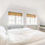 Schlafzimmer mit Dachschräge, zwei Fenstern und weißem Bett.