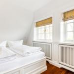 Schlafzimmer mit Doppelbett, weißen Wänden und zwei Fenstern mit bunten Rollläden.