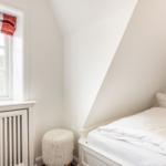 Ein Schlafzimmer mit weißem Bett, Fenster mit Rollladen und Fellhocker.