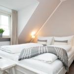 Schlafzimmer mit Dachschrägen, weißem Bett und Nachttisch mit Lampe.