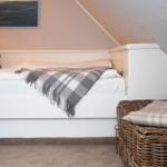 Schlafzimmer mit Dachschräge, weißem Bett und Korb mit Decke.