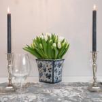 Tisch mit Blumen, Kerzen und Gläsern. Blumenvase mit blau-weißem Muster.