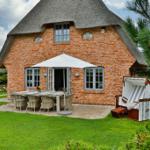 Rotes Backsteinhaus mit Strohdach, Garten mit Tisch, Stühlen und Strandkorb.