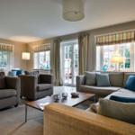 Wohnzimmer mit Sofa, Sesseln und Fenstern mit Gardinen.