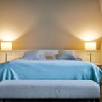 Schlafzimmer mit Bett, blauer Decke und zwei Nachttischen mit Lampen.