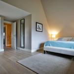 Schlafzimmer mit Bett, Teppich und Blick in Bad und Flur.