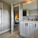 Badezimmer mit Waschbecken, Spiegel und Handtuchheizkörper. Tür führt in Schlafzimmer.