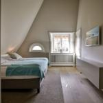 Schlafzimmer mit Dachschräge, Bett, Fenster und Wandbild.