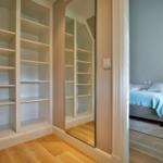 Schlafzimmer mit Bett, Nachttisch und Spiegelschrank. Holzboden und Wandspiegel sichtbar.