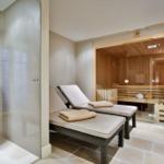 Dusche mit Mosaikwand, zwei Liegestühle und Sauna mit Holzverkleidung.