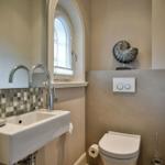 Badezimmer mit Waschbecken, Spiegel und Toilette. Fenster und Mosaikwand.