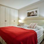 Schlafzimmer mit Bett, rotem Decken, Schrank und Nachttisch mit Lampe.