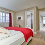 Schlafzimmer mit Bett, Fenster und Blick in Bad und Flur.