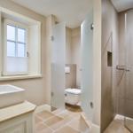 Badezimmer mit Dusche, Toilette und Waschbecken. Fenster mit Jalousie.