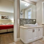 Badezimmer mit Waschbecken und Spiegel. Im Hintergrund Schlafzimmer mit Bett.