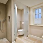Dusche mit Mosaikfliesen, Toilette hinter Glaswand und Waschtisch mit Fenster.