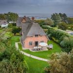 Rotes Backsteinhaus mit Strohdach, Garten und Blick aufs Meer.