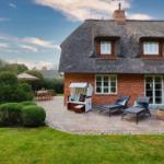 Haus mit Strohdach, Terrasse, Liegen und Garten.