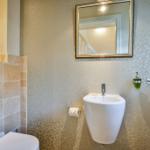 Badezimmer mit Wandspiegel, Hängewaschbecken und Toilette.