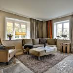 Wohnzimmer mit Sofa, Sessel, Teppich und Fenstern mit Vorhängen.