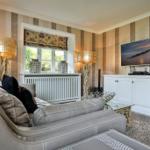 Ein Wohnzimmer mit grauem Sofa, TV und gestreifter Wandtapete.