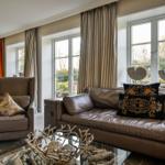 Wohnzimmer mit Ledersofa, Sessel und Glas-Tisch. Fenster mit Gardinen und Dekoration.