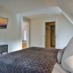 Schlafzimmer mit Bett, Nachttisch und Wand-TV. Blick in Badezimmer und Kleiderschrank.