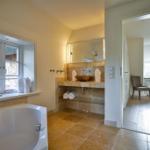 Badezimmer mit Badewanne, Waschtisch und Blick in Schlafzimmer.