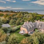 Haus mit Strohdach, Garten und Blick aufs Wasser.