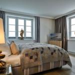 Schlafzimmer mit Bett, Fenstern, Lampe und Fernseher.