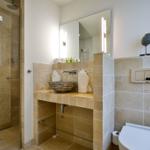 Badezimmer mit Dusche, Waschbecken und Toilette. Steinfliesen und Spiegelschrank.