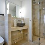 Badezimmer mit Dusche, Waschbecken und Toilette. Steinwand und Spiegel sichtbar.