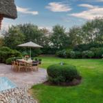 Roter Backsteinbau mit Garten, Tisch und Stühle unter Sonnenschirm.