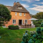 Haus mit Strohdach und Garten mit Terrasse und Tisch.