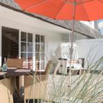 Terrasse mit Tisch, Stühlen und orangefarbenem Sonnenschirm. Hintergrund: weißes Haus mit Schiebetür.