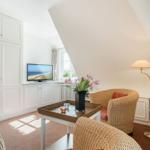 Wohnraum mit Schrank, Fernseher, Sessel und Tisch unter Dachschräge.
