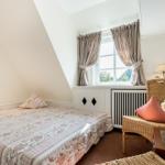 Schlafzimmer mit Dachschrägen, Bett, Fenster und Wickerstuhl.