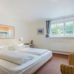 Schlafzimmer mit Bett, Fenster und Wickerstuhl.