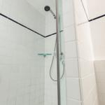 Dusche mit Glaswand, weißen Fliesen und dunkler Zierleiste