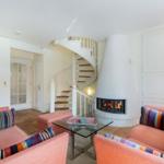 Wohnzimmer mit Kamin, Spiral-Treppe und orangefarbenen Sofas.