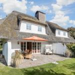 Haus mit Strohdach, Terrasse mit Sonnenschirm und Garten.