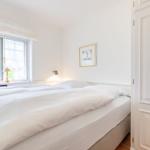 A bedroom with a white bed, window, and door.
