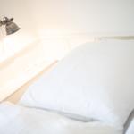 Headboard with white bedding and wall lamp.