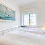 Bedroom with white bed, window, and wall painting of a sailboat.
