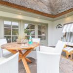 Terrace with table, chairs, and lounge under thatched roof.