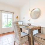 Dining room with rustic table, two wicker chairs, and view to the garden.