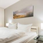 Schlafzimmer mit weißem Bett, Nachttisch und Wandbild.